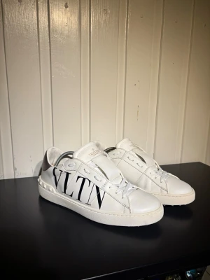 Vita Valentino VLTN sneakers - Säljer ett par vita Valentino open sneakers med VLTN-logga i svart på sidan. Skorna har endast testats några få gånger och är i grymt skick. Skorna är i storlek 41 men passar även 42!! Hör av dig vid frågor och funderingar!!