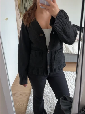 Svart kofta med knappar och fickor - Mysig svart kofta från lager 157 med v-ringning och stora bruna knappar framtill. Koftan har två fickor framtill och ger en lite oversized känsla! Väldigt mysig och mjuk!