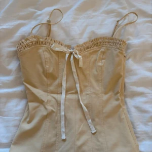 Gul topp från Zara - Säljer en gul topp med smala justerbara axelband och söt snörning framtill. Modellen har rynkad kant upptill och är figurnära med markerade sömmar för en snygg siluett. Perfekt att styla med jeans eller kjol för en trendig look. (Prislapp kvar!)