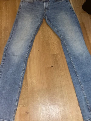 Ljusblå raka jeans från smog  - Säljer ett par ljusblå jeans från smog med rak passform och klassisk femficksdesign. Jeansen har en snygg tvättad look och är tillverkade i denim. Perfekta för en avslappnad och trendig stil.