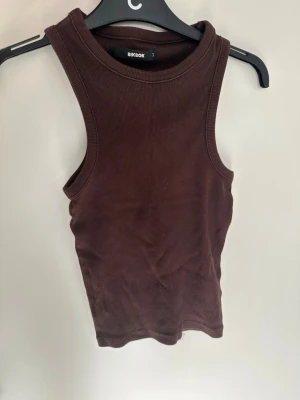 Brun ribbad tanktop från BikBok - Säljer en brun ribbad tanktop från BikBok. Toppen har breda axelband och en rund halsringning. Materialet är stretchigt och bekvämt, perfekt för att matcha med jeans eller kjol. Enkel och stilren design som passar till många outfits.