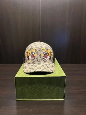Gucci keps med tigerbrodyr - Säljer en snygg Gucci keps med klassiskt GG-mönster i beige och brunt. Framtill finns broderade tigrar i gult, svart och rött. Baksidan är i svart mesh för extra ventilation. Perfekt för dig som vill sticka ut med en exklusiv accessoar.