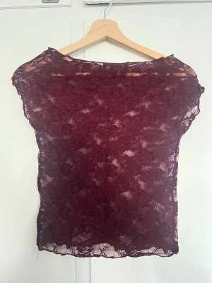 Vinröd spetsblus med blommönster - Säljer en vinröd blus i genomskinlig spets med blommigt mönster. Toppen har en boatneck modell💗💗