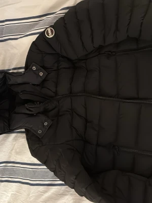 Svart pufferjacka från colmar - Säljer en svart pufferjacka från colmar med huva och dragkedja framtill. Jackan har två sidofickor med dragkedja och en patch med colmar-logga på ärmen. Perfekt för kalla dagar och riktigt skön att bära tack vare det vadderade materialet.