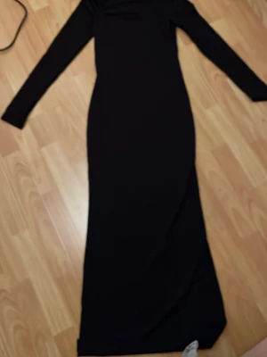 Svart långärmad långklänning Gina Tricot - Stilren svart långklänning från Gina Tricot med lång ärm och figurnära passform. Klänningen har en enkel, elegant design och är perfekt för dig som gillar en klassisk look. Tillverkad i mjukt material som känns bekvämt mot huden.