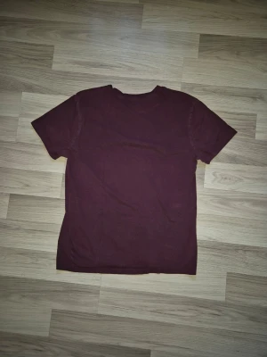 Vinröd t-shirt från H&M - En enkel och stilren vinröd t-shirt från H&M med rund halsringning och korta ärmar. Tillverkad i mjuk bomull som känns skön mot huden. Perfekt basplagg att matcha med jeans.