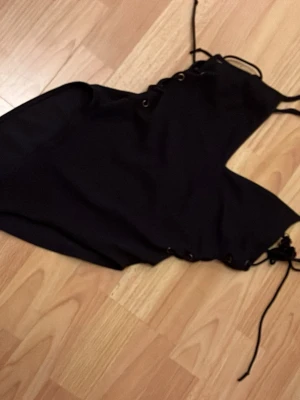 Svart baddräkt med snörning Topshop - Snygg svart baddräkt från Topshop med trendig snörning i sidorna och vid axelbanden. Modellen har hög skärning vid benen och öppen rygg. Tillverkad i stretchigt material som sitter bekvämt och formar sig efter kroppen. Perfekt för stranden eller poolen.