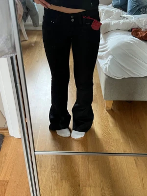 Svarta bootcut jeans med detaljer - Säljer ett par svarta bootcut jeans med låg midja och dekorativa sömmar baktill. Jeansen har dubbla knappar och fickor både fram och bak med silverfärgade detaljer. Storlek 32/34(xxs/xs). De är helt oanvända med lapp kvar. Köpta i London. Kom med prisförslag