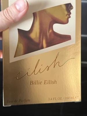 Eilish Eau de Parfum Billie Eilish, 100 ml. Helt ny - Eilish Eau de Parfum från Billie Eilish i en unik, bronsfärgad flaska formad som en byst. Förpackningen är guldig med konstnärlig design och signatur. Innehåller 100 ml och är en parfym som sticker ut både i doft och utseende.