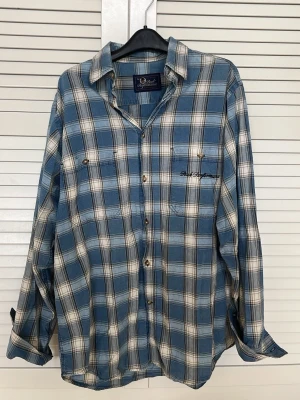 Blåvit rutig skjorta med knappar - Snygg blå och vit rutig vintage skjorta från Peak Performance med klassisk krage och knäppning framtill. OBS! avslappnad passform.