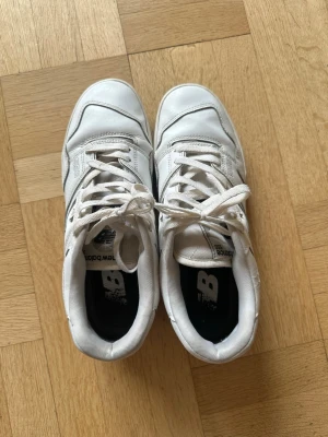 Vita New Balance 550 sneakers - Säljer ett par klassiska vita New Balance 550 sneakers med lågt skaft. Skorna har snygga detaljer, perforerade partier på sidorna och tydlig logga på sidan. Tillverkade i läder med gummisula och vita skosnören. Perfekta för dig som gillar stilrena och sportiga sneakers. Använda flitigt och har därav en del skavanker, som visas på bilderna. 