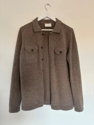 Brun overshirt Bruun & Stengade  - Snygg brun overshirt i mjuk ullmix. Klassisk rak modell med krage, knäppning framtill och två bröstfickor med lock och knapp. Perfekt lager-på-lager-plagg för kyligare dagar och enkel att styla till olika outfits. NY PRIS 1300kr 
