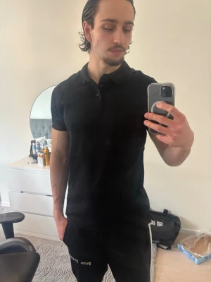 Svart pikétröja med krage - Säljer en stilren svart pikétröja med klassisk krage och knappar framtill. Tröjan har korta ärmar och en slim passform som sitter snyggt på kroppen. Perfekt för dig som gillar en clean och enkel look.