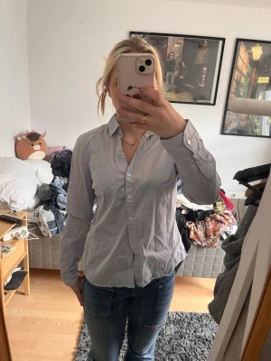 Ljusblå klassisk skjorta - Säljer en ljusblå skjorta med klassisk krage och knappar framtill. Skjortan har lång ärm med knapp vid manschetten och är tillverkad i ett tunt, mjukt bomullstyg. Perfekt till jeans eller kjol för en clean look.