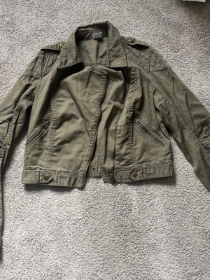 Grön vårjacka - Säljer den här fina vårjackan från gina. Skulle säga att modellen är lite som en skinnjacka men i bomull. Den är i storlek 38 men ganska liten i storlek.🤍