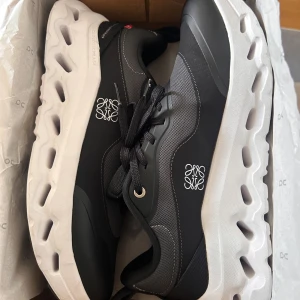 On x Loewe Cloud – lyx + komfort (nyskick) - Säljer ett par exklusiva sneakers från samarbetet mellan On och Loewe. Modellen kombinerar sportig komfort med lyxig design.  Skorna är i mycket fint skick och har endast använts 3 gånger, vilket gör att de känns nästan som nya. De har en stilren svart ovandel och en kraftig vit sula med On’s karakteristiska CloudTec-teknologi som ger väldigt bra dämpning och komfort.  Perfekta både för vardag och en mer uppklädd streetwear-look.  • Skick: Nästan nyskick • Användning: Endast 3 ggr • Färg: Svart