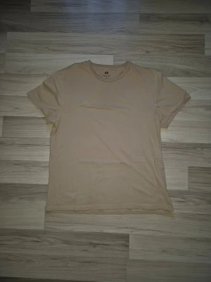Beige basic t-shirt från H&M - En enkel beige t-shirt från H&M med rund hals och korta ärmar. Tillverkad i mjuk bomull för en skön känsla och avslappnad passform. Perfekt att matcha med jeans eller shorts för en clean och stilren look.