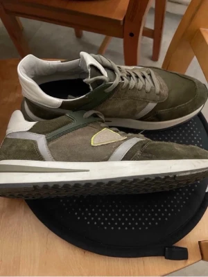 Phillipe model storlek 42 - Snygga gröna sneakers från Le Coq Sportif med vita och grå detaljer samt en gul kant runt loggan på sidan. Skorna har en låg profil, klassisk snörning och en vit sula med mönstrad undersida. Materialet är en mix av mocka och textil.