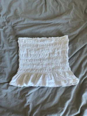 Vit bandeau tubtopp med volang - Supersöt vit bandeau tubtopp från Gina tricot. Passar perfekt till en sommardag eller när man vill klä upp sig. Säljer pga att den inte passade, aldrig använd. Väldigt skönt och luftigt material. Hör av dig vid frågor!💗