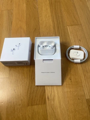 Apple AirPods 2 Pro med laddningsetui - Säljer ett par vita Apple AirPods Pro med tillhörande laddningsetui och USB-C kabel. Hörlurarna är trådlösa och har en stilren design med silikonpluppar för extra komfort. Perfekt för dig som vill ha bra ljud och smidig anslutning till din iPhone.