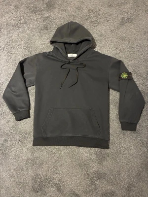 Svart hoodie från Stone Island - Säljer en svart hoodie från Stone Island med klassisk huva och dragsnören. Den har en stor magficka och den ikoniska Stone Island patchen på vänster ärm. Modellen på bild 2 är 165cm lång och väger runt 55kg ✅ hör av er vid funderingar och frågor 