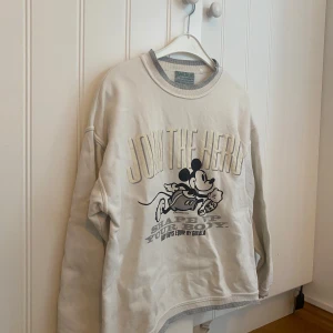 Musse pigg sweatshirt - Säljer en portugisisk vintage sweatshirt med tryck av Mickey Mouse och texten 'JOIN THE HERO' framtill. Tröjan har rund hals med grå ribbade detaljer och är perfekt för en avslappnad stil.