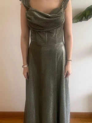 Glittrig långklänning i grönt. - Säljer en elegant glittrig långklänning i grönt med draperad halsringning och offshoulder-design. Klänningen har en figurnära passning upptill och faller snyggt ner mot golvet. Perfekt för dig som vill sticka ut med en lyxig look. Den är M men passar S också.