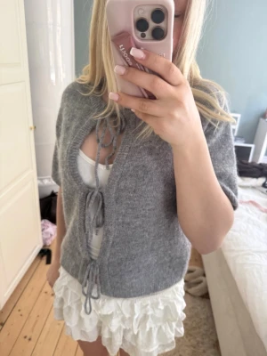 Grå stickad kofta med knytband - Säljer en grå stickad kofta med korta ärmar och knytband framtill. Jättebra till våren och sena sommar kvällar. Säljer pga att jag tycker inte att den sitter bra på mig