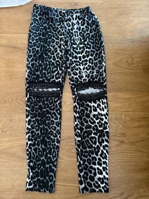 Leopardmönstrade leggings med spets - Snygga leggings med leopardmönster i svart och vitt. De har coola spetsdetaljer över knäna som ger en extra edge. Elastisk midja för skön passform. Perfekta för dig som vill sticka ut och gillar djurmönster. Storlek S-M !