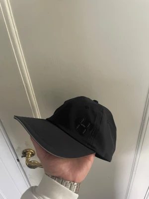 Svart keps från Haglöfs - Snygg svart keps från Haglöfs med böjd skärm on size storlek S. Kepsen har diskret Haglöfs-logga framtill och broderad text bak. Tillverkad i lätt och slitstarkt material, perfekt för en sportig och avslappnad stil. Helt ny från Haglöfs hemsida, gick ej o returnera då lappar hade tagits av
