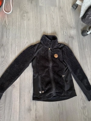 Svart teddyjacka med dragkedja - Snygg svart teddytröja från JH collection med mjuk, fluffig yta och hög krage. Jackan har hel dragkedja framtill. Perfekt för kyliga dagar i stallet. Säljer då den är för liten för mig. Pris kan diskuteras vid snabbt köp💕