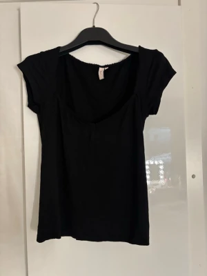 Svart topp med spetskant från Nelly  - En svart topp från Nelly med korta ärmar och rundad urringning. Toppen har en söt spetskant längs halsringningen och är tillverkad i ett mjukt och skönt material som sitter bekvämt. Aldrig använd💕💕