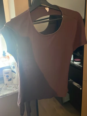 Brun kortärmad topp med knyt - öppen rygg, Snygg brun topp med korta ärmar och rund halsringning. Toppen har en cool knytdetalj i sidan som ger en trendig look. Perfekt att styla med jeans eller kjol för en avslappnad vibe.