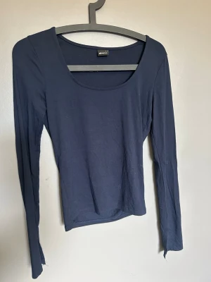 Mörkblå långärmad topp från Gina Tricot - Säljer en mörkblå långärmad topp från Gina Tricot med rundad halsringning och slits vid ärmslut. Toppens passform är slim och den är tillverkad i mjuk bomull, perfekt för att skapa en clean och enkel look.