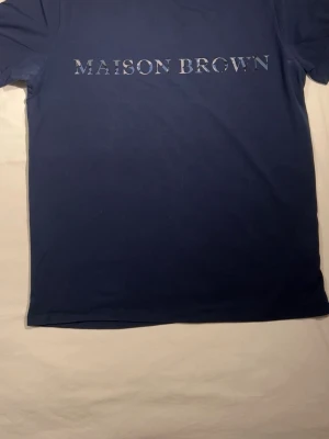 Blå t-shirt från Maison Brown - Snygg mörkblå t-shirt från Maison Brown med klassisk passform och korta ärmar. Tryck med logotypen på bröstet. Perfekt för dig som gillar stilrena plagg med diskret branding. Materialet känns mjukt och bekvämt mot huden.