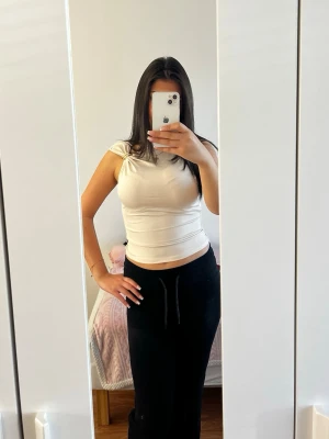 Beige ärmlös topp med gulddetalj - Säljer en beige, tight och ärmlös topp med snygg guldfärgad ringdetalj på ena axeln. Toppen har en croppad passform och är tillverkad i ett mjukt, stretchigt material som sitter skönt mot kroppen. Perfekt för dig som gillar stilrena och trendiga plagg.