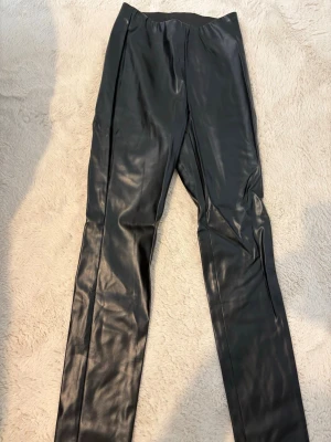 Oanvända Svarta leggings i skinnimitation Gina Tricot - Aldrig använda. Snygga svarta leggings i skinnimitation från Gina Tricot. De har en tight passform och bred resår i midjan för extra komfort. Perfekta att styla med oversized tröjor eller kavaj för en trendig look.