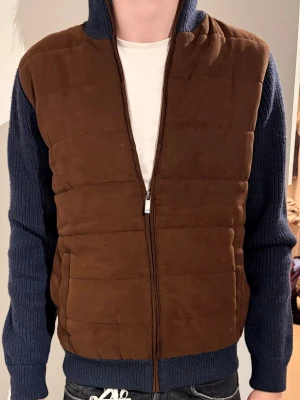 Spada Roma cardigan - Säljer en unik cardiganjacka med quiltad brun framsida och stickade blå ärmar samt rygg. Jackan har dragkedja framtill och hög krage. Perfekt för dig som vill ha en kombination av stil och komfort. Materialet är en mix av stickat tyg och vadderad front.