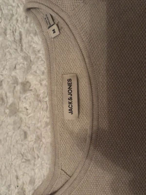 Beige tröja från Jack & Jones - Snygg beige tröja från Jack & Jones i storlek M. Tröjan har rund halsringning, lång ärm och är tillverkad i ett mjukt, tunt material med diskret struktur. Perfekt att matcha med jeans eller chinos för en clean look. Använd 1-2 gånger 