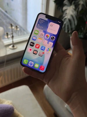 Iphone 13 mini (NYTT BATTERI) - Säljer en svart iPhone 13 med stilren design och rundade hörn. Telefonen har en stor skärm, två bakre kameror och Apples logga på baksidan. Tillverkad i glas och aluminium, perfekt för dig som gillar snygg och modern teknik.