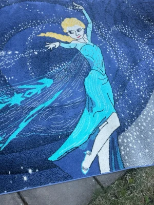 Blå matta med frostmotiv - Säljer en stor matta med motiv av en dansande figur i blå klänning och blont hår, omgiven av snöflingor och stjärnor. Mattan har olika nyanser av blått och turkos, med detaljer i vitt och gult. Perfekt som dekor i barnrum eller för dig som gillar frosttema. Matta mått är 150x220