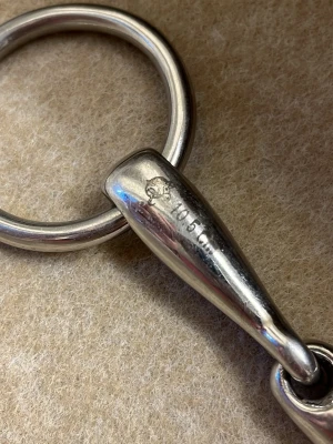 Metallbett till häst Sprenger - Säljer ett tredelat bett i metall från Sprenger, perfekt till hästutrustning. Bettet är silverfärgat och har runda ringar i båda ändar samt en rörlig mittdel. Märkt med storlek 105 -10,5cm och Sprenger-logga.