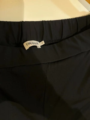 Svarta mjukisbyxor från Filippa K - Svarta kostym  från Filippa K med elastisk midja. Byxorna har en enkel och stilren design, perfekta för en avslappnad look. Tillverkade i ett mjukt och bekvämt material som känns skönt mot huden.