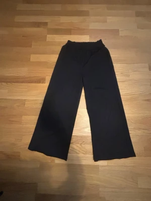 Svarta vida leggings med resårmidja - Säljer ett par svarta leggings med breda ben och resår i midjan. De har en enkel och stilren look, perfekta för en avslappnad outfit. Materialet känns mjukt och stretchigt, vilket gör dem riktigt bekväma att bära.