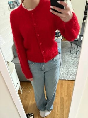 Röd fluffig kofta med knappar - Säljer en superfin röd kofta med rund hals då jag inte använder den. Koftan har matchande röda knappar framtill. Det står inget märke eller storlek på, men passar mig som brukar ha S. 