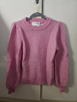 Rosa stickad tröja från Selected Femme - Supermysig och gullig rosa stickad tröja från Selected Femme i storlek XS. Tröjan har en rund halsringning, ballongärmar och ribbade muddar. Passar lika bra till jeans som till kjol. Mycket bra skick och aldrig använd. Känns något sträv mot huden så rekommenderas med ett linne/t-shirt under för bästa komfort. Nypris runt 700 kr. Säljer den då jag inte får någon användning för den.