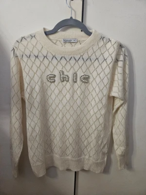 Vit stickad tröja med pärltext - Jag säljer denna jättegulliga beigea stickade tröjan från Fullamoda med pärlbroderade bokstäver 'chic' framtill. Rund hals och långa ärmar. Aldrig använd och därför i mycket bra skick. Jättefin att matcha till exempel jeans, linnebyxor eller kostymbyxor. Den sitter som en xs/xxs. 💓