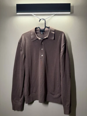 Brun långärmad pikétröja H&M - Snygg brun långärmad pikétröja med klassisk krage och tre knappar framtill. Tillverkad i mjukt, tunt material som passar perfekt för lager på lager. Enkel och stilren design som funkar till det mesta.