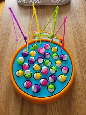 Fiskespel med färgglada fiskar - Roligt fiskespel med snurrande blå spelplan och fiskar i lila, rosa, gul och grön färg. Fyra fiskespön i olika färger ingår. Elektroniskt fiskespel i jättefint skick.  Inget att anmärka på, testat innan det las ut till försäljning.