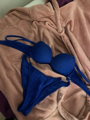 Blå bikini från Calzedonia med detaljer - Snygg blå bikini från Calzedonia med vadderad bygel-bh och matchande trosa. Bikinin har ett diskret geometriskt mönster i tyget och guldfärgade metalldetaljer på trosan. Perfekt för stranden eller poolen!